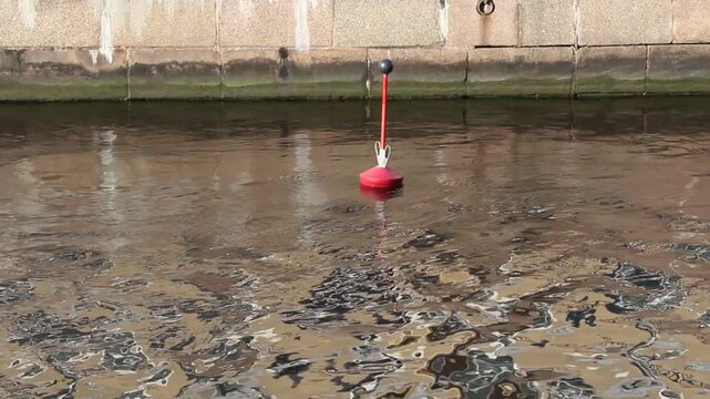 Red Buoy Floating on Calm Water in Urban City Canal.

