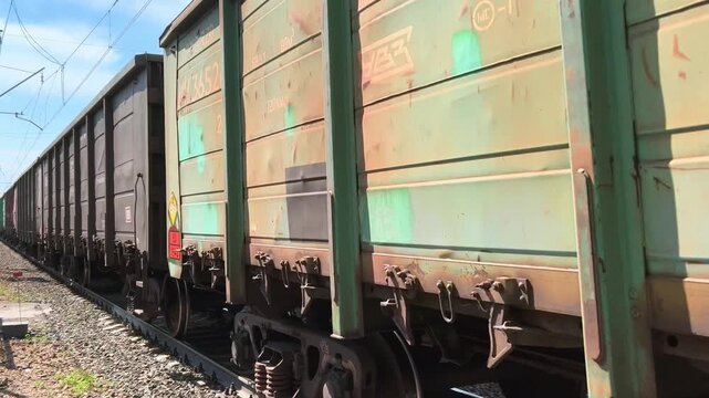 Green freight train cargo wagons rolling along railway line side view