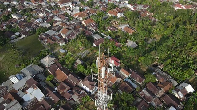 Aerial View of Large Telecommunication Tower Standing Amid a Densely Populated Rural Settlement in Indonesia. Telecommunications Infrastructure Rises Above Green Highland.