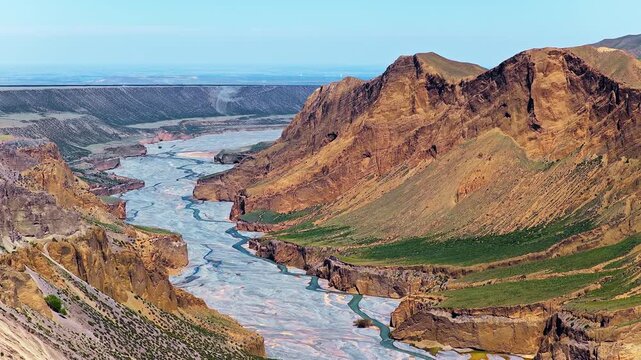 Aerial view of a winding braided river flowing through a deep rocky canyon under a clear blue sky in Anjihai Grand Canyon, Xinjiang, China