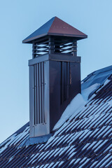 Fototapeta premium Snow covers roof tiles beneath a chimney with red-topped vent