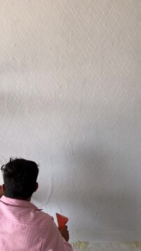 Worker applying wallpaper adhesive to a textured white wall using a tool