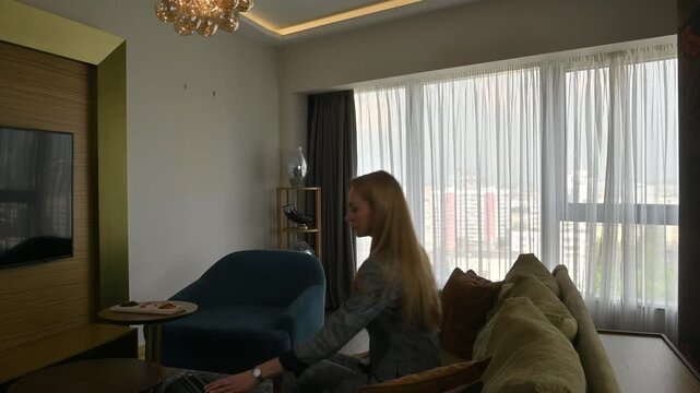 Businesswoman entering a modern hotel suite with her luggage after a business trip, sitting down on the couch to rest and relax before her next meeting or flight