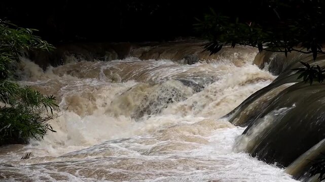 Rushing Waters: A powerful torrent of muddy water cascades over natural rock formations, creating a dynamic display of nature's raw energy and force.