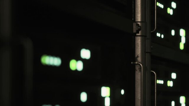 Small green lights blink on digital displays in a server room. The room is dark, and the lights are the main source of illumination. The setting suggests a busy data processing area.