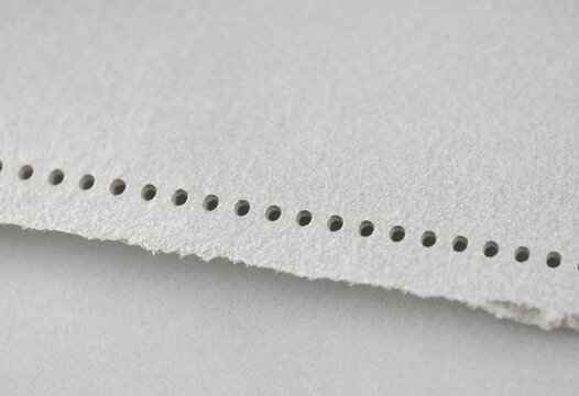 Macro close up shot of a piece of white perforated paper with a rough torn edge
