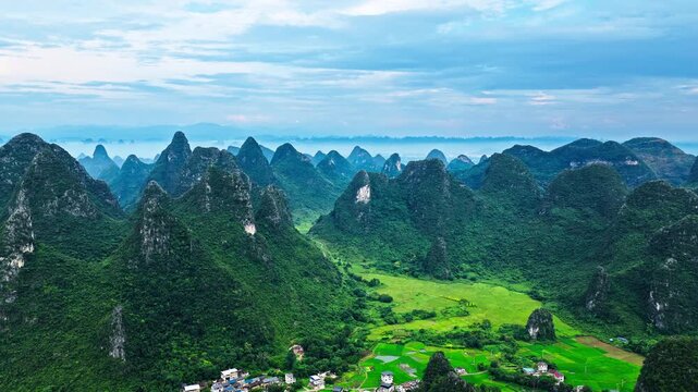Aerial view of karst valley with green rice fields and a rural village surrounded by mountains in Guilin, China