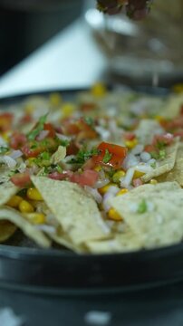 Vertical video close up of chef hands sprinkling chopped tomato onion salsa over crispy corn nachos on plate