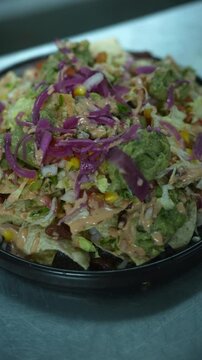 Vertical video close up of loaded crispy tortilla nachos with guacamole salsa chipotle sauce and purple cabbage garnish
