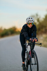 Fototapeta premium Female Road Cyclist Training on Open Road Wearing Helmet and Sunglasses in Aerodynamic Position