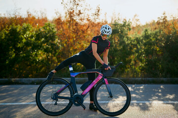 Fototapeta premium Female Cyclist Stretching On Aerodynamic Road Bike Before Training Ride In Autumn Sunrise