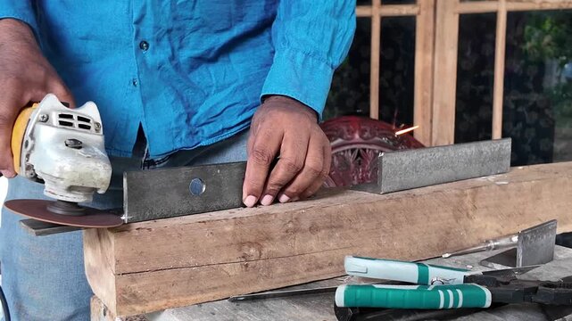 Industrial worker cutting a thick steel bar with a handheld angle grinder, producing bright sparks during metal fabrication work.
