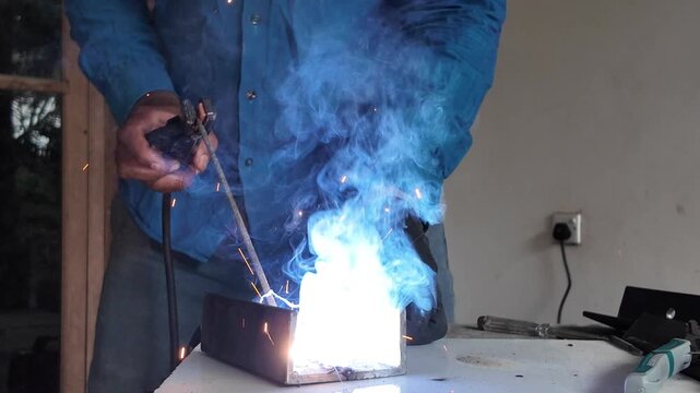 Skilled worker welding metal components using protective equipment, with intense sparks and bright welding light during fabrication.