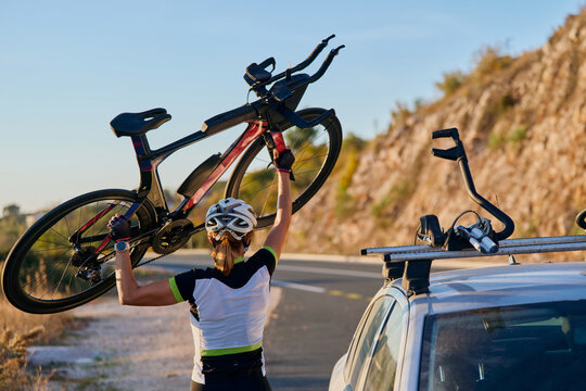 Cyclist Lifting Road Bike Onto Car Roof Rack After Training Ride On Scenic Mountain Road