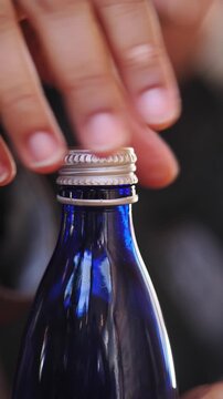 Hand opening a blue glass bottle