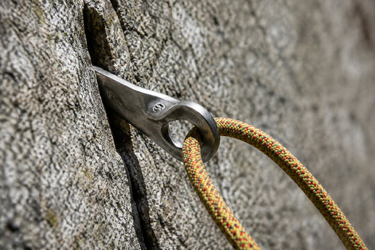 A steel climbing piton in granite with a rope, natural daylight.