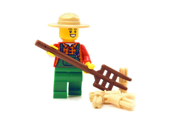 Fototapeta premium Lego minifigure of happy farmer with pitchfork or hayfork is doing isolated on white. Editorial illustrative image of popular plastic toy.