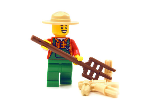 Lego minifigure of happy farmer with pitchfork or hayfork is doing isolated on white. Editorial illustrative image of popular plastic toy.