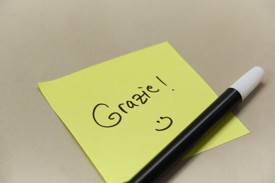 Handwritten Grazie Thank You text in Italian on yellow sticky note with marker pen