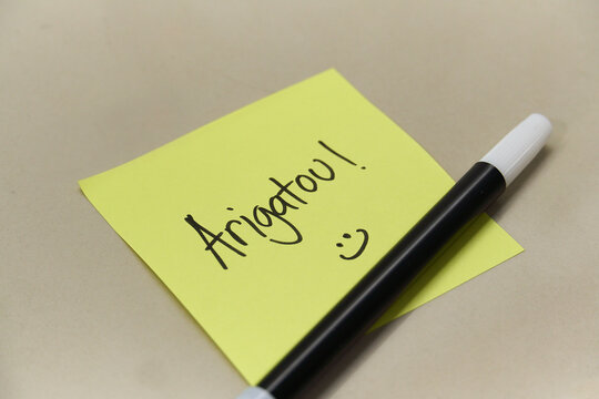 Handwritten Arigatou Thank You text in Japanese on yellow sticky note with marker pen