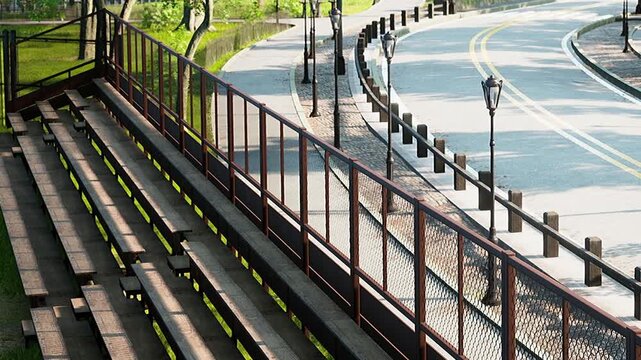 People walk along the paved path beside a tree lined road. Street lamps line the route, providing light during evening hours. The green area invites leisure and relaxation.