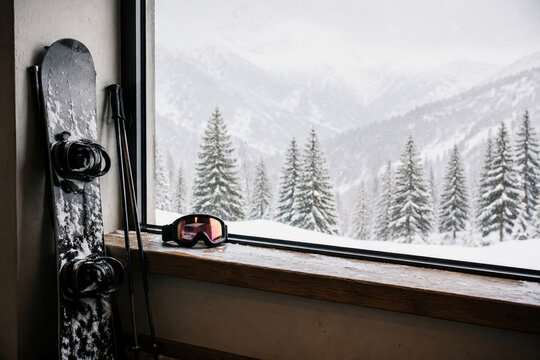 Snowboard, ski poles, and goggles on window ledge for winter sports and alpine cabin atmosphere