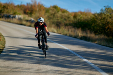 Naklejka premium Cyclist Riding Road Bike Fast On Winding Country Road During Sunny Autumn Training