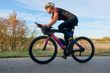Fototapeta premium Female Cyclist Riding Road Bike In Aerodynamic Position On Countryside Pavement At Sunrise