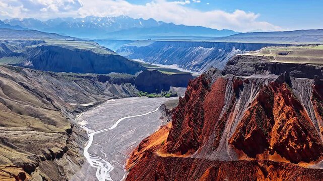 Aerial view of dramatic red rock formations and a winding riverbed in Anjihai Grand Canyon, Xinjiang, China