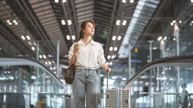 Young adult business asian woman to transit with travel luggage at international airport terminal on the go with financial freedom