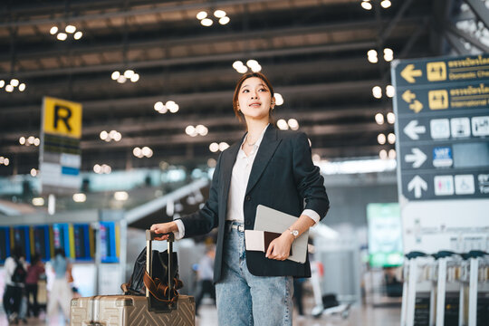 Young adult asian businesswoman wear blazer with luggage business trip at international airport terminal departure platform