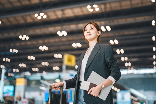 Young adult asian businesswoman wear blazer with luggage business trip at international airport terminal departure platform