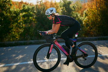 Fototapeta premium Female Cyclist Training on a Road Bike During Sunny Autumn Morning for Triathlon Fitness and Endurance