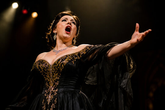 Opera singer on stage with dramatic lighting.