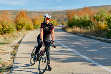 Naklejka premium Female Cyclist Training On Scenic Autumn Road With Road Bike And Helmet