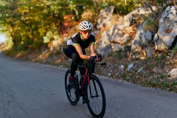 Fototapeta premium Female Cyclist Training on a Road Bike Through Autumn Countryside at Sunset
