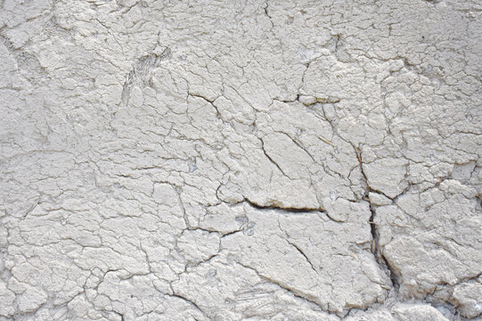 Close-up of a weathered rustic mud wall surface made of clay, soil, and dry straw mixture with deep natural cracks and an organic rough finish