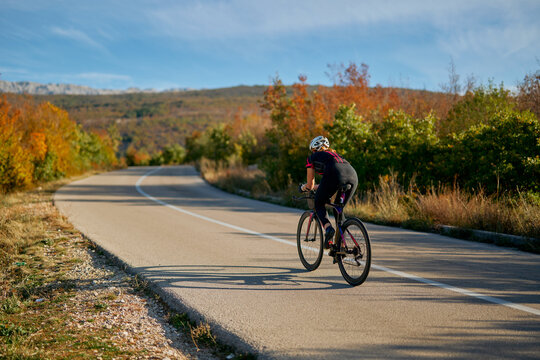 Road Cyclist Training Through Autumn Countryside On Empty Winding Road For Endurance Fitness