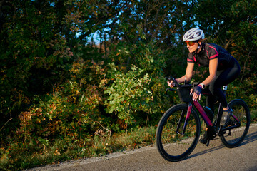 Fototapeta premium Female Cyclist Riding Road Bike Along Tree-Lined Country Road During Outdoor Training