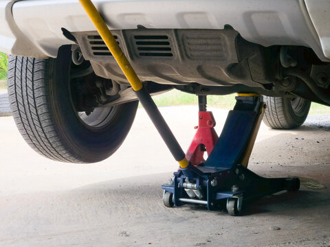 Hydraulic floor jack and red safety jack stand supporting lifted car during underbody maintenance