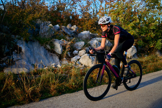 Female Cyclist Riding Road Bike Outdoors in Autumn Landscape Training for Fitness and Endurance