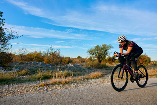 Female Cyclist Riding Road Bike Outdoors on Country Road at Sunset for Fitness Training