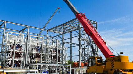 A yellow construction crane with a long red boom is used for lifting and installing metal structures. © SGr
