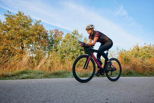 Female Cyclist Training On Road Bike During Sunrise Outdoor Fitness Ride In Autumn Countryside