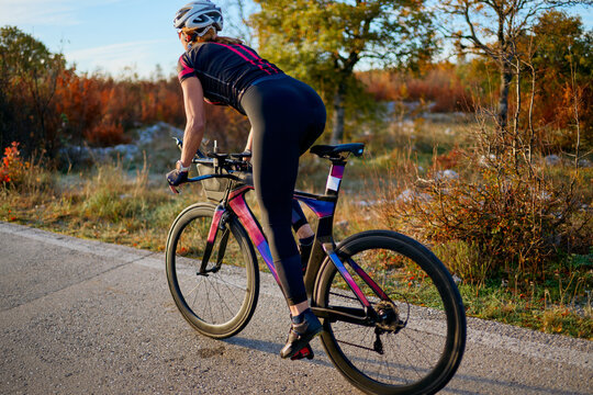 Female Cyclist Riding Road Bike Outdoors at Sunset in Autumn Countryside for Fitness Training