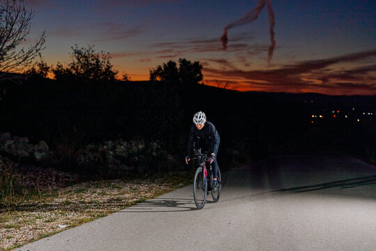 Night Road Cyclist Training At Sunset Wearing Helmet And Reflective Gear On Empty Country Road