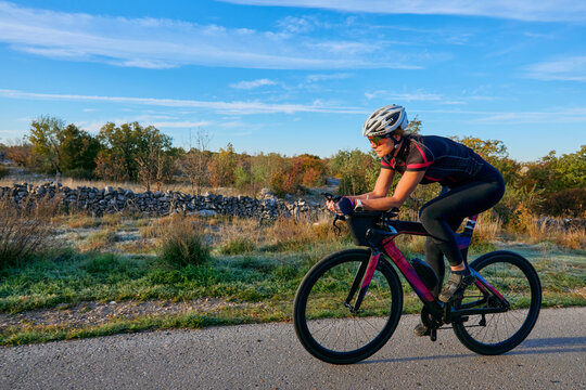Female Cyclist Training on Road Bike Outdoors at Sunrise - Fitness Cycling Athlete Riding