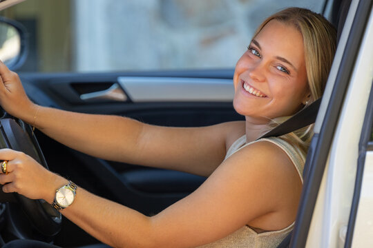 Young smiling woman driving a car, looking back over her shoulder with a happy expression, enjoying a road trip adventure