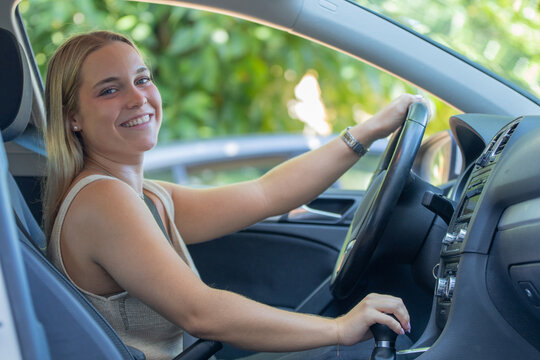 Young smiling woman driving a car, holding steering wheel and gear shift, happy female driver enjoying road trip