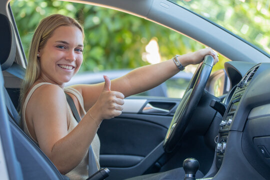 Happy young woman giving thumbs up while sitting in driver's seat of car, smiling confidently with hand on steering wheel, new driver success concept